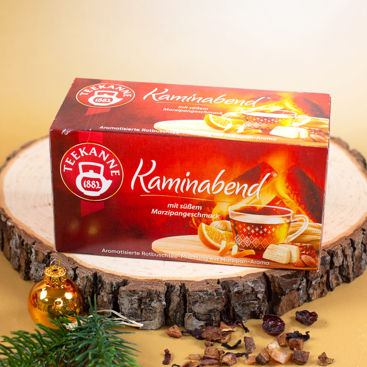 Teekanne Kaminabend Rotbuschtee mit Marzipangeschmack auf Holzscheibe mit Weihnachtskugel, Tannenzweig und Tee-Dekoration