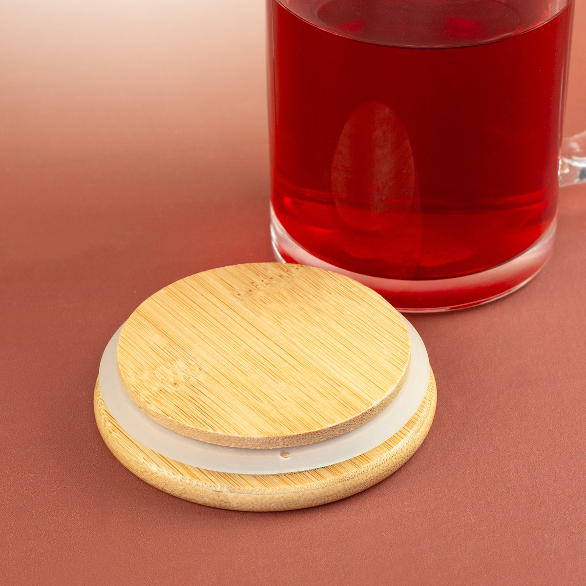 Unterseite des Bambusdeckels mit Dichtungsring vor einer Glastasse mit rotem Tee