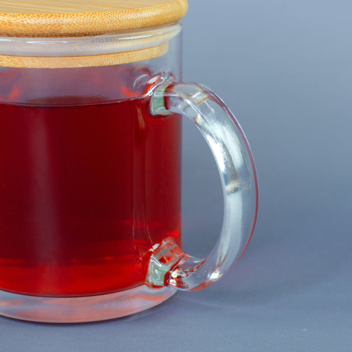 Detailaufnahme des transparenten Henkels der Glastasse mit rotem Tee und aufgesetztem Bambusdeckel