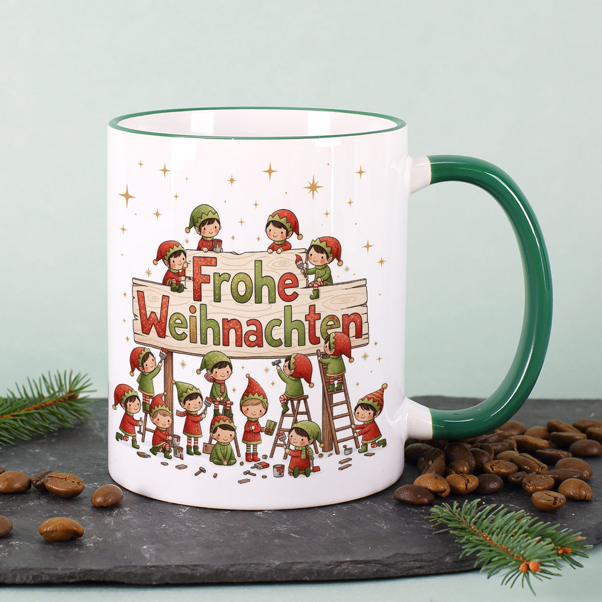 Wichteltasse auf einer Schieferplatte; Motiv zeigt Wichtel, die am Holzschild „Frohe Weihnachten“ werkeln.