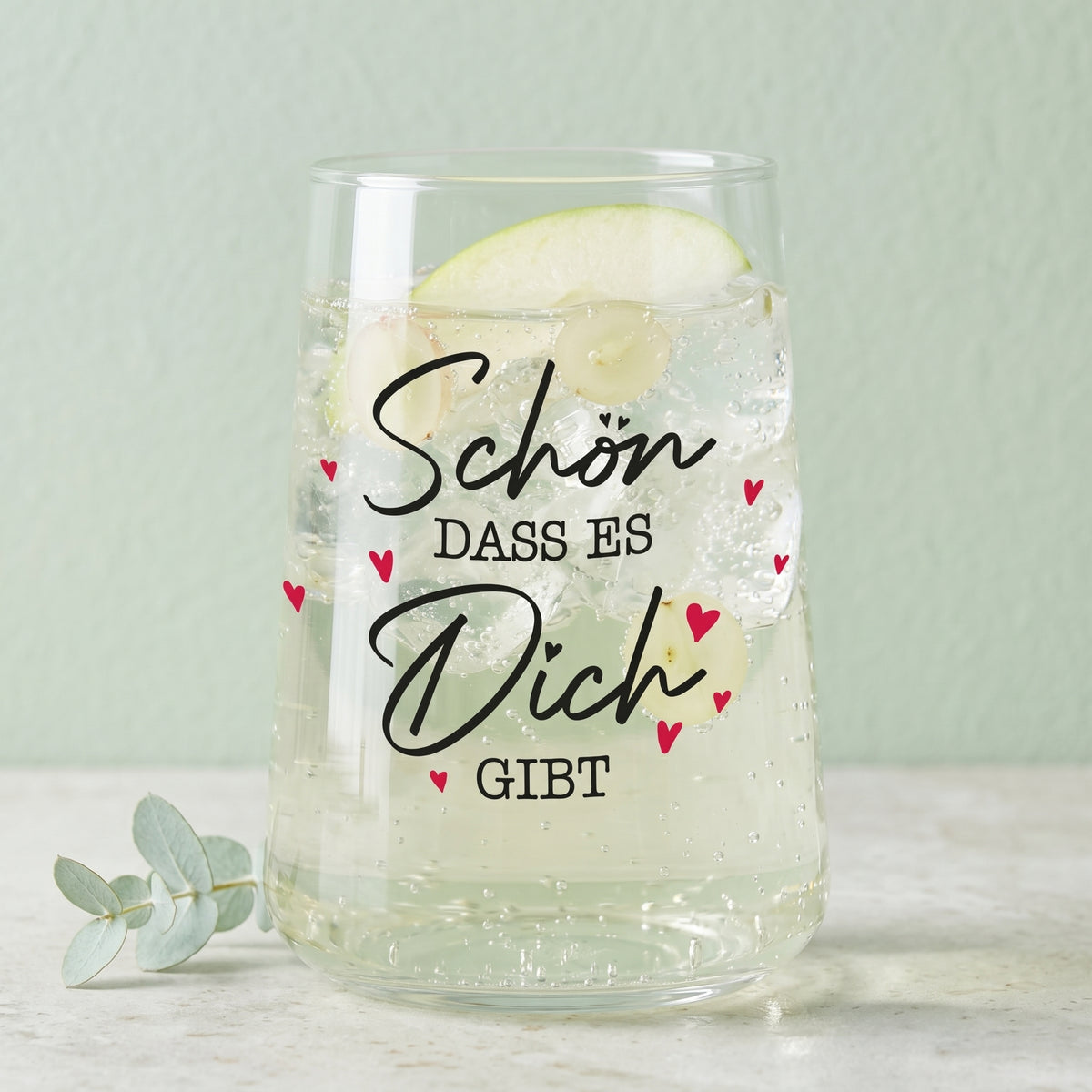 Trinkglas mit Aufdruck Schön dass es Dich gibt, gefüllt mit hellem Getränk und grüner Dekoration