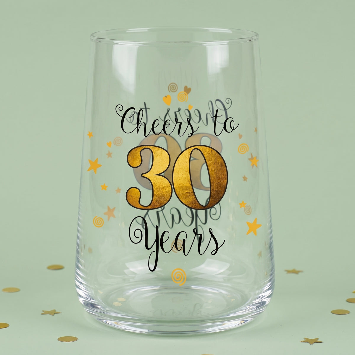 Leeres Trinkglas mit Cheers to 30 Years Aufdruck, goldener 30 und Sternen auf grünem Hintergrund