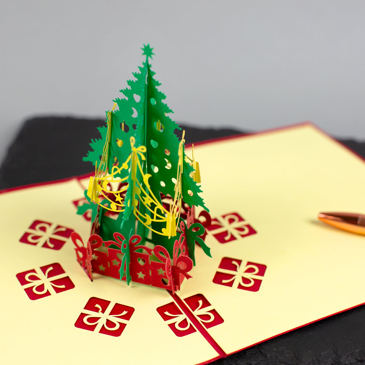 Aufgeklappte 3D-Weihnachtskarte mit grünem Tannenbaum und roten Geschenk-Motiven aus Papier.