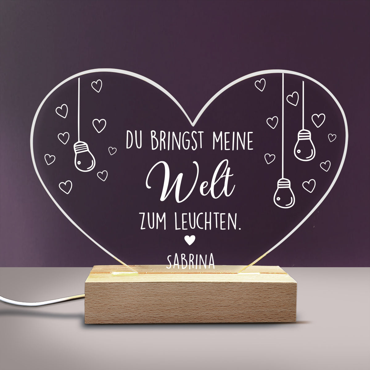 Personalisierte Acryl-LED-Lampe in Herzform mit Spruch „Du bringst meine Welt zum Leuchten“ und Name „Sabrina“ auf Holzsockel