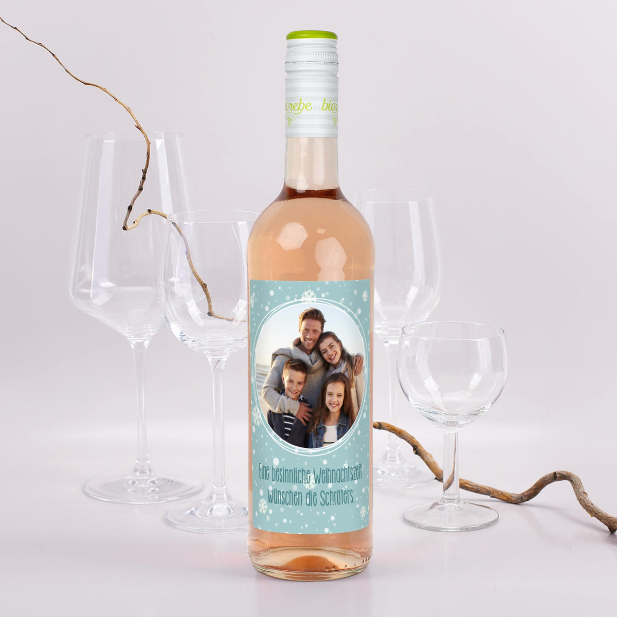 Personalisierte Roséweinflasche mit Schneeflocken-Etikett, eigenem Foto und Weihnachtsgruß – Szene mit Gläsern