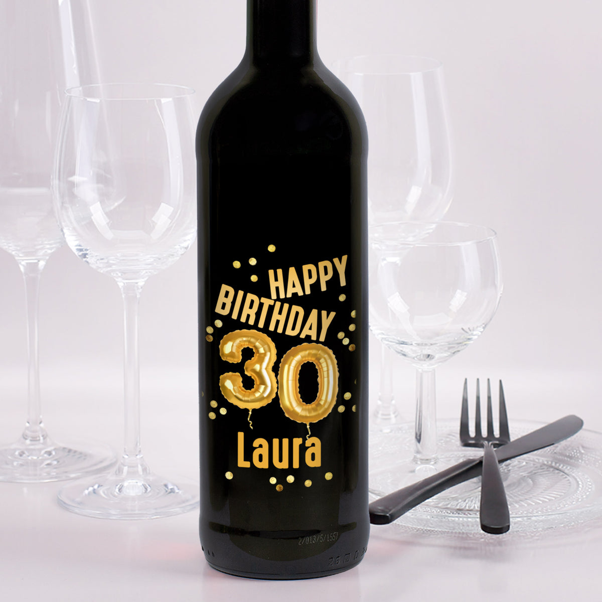 Weinflasche mit schwarzem Etikett „Happy Birthday 30 Laura“ in goldener Ballon-Optik, goldene Konfetti als Verzierung