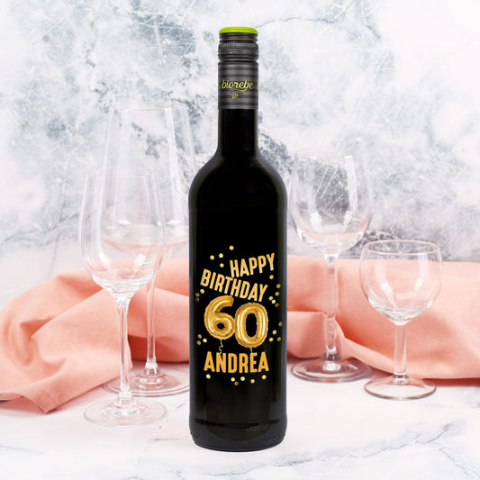 Weinflasche mit schwarzem Etikett zum 60. Geburtstag, goldene Ballons „60“, Name Andrea, Hintergrund mit rosa Stoff und Weingläsern