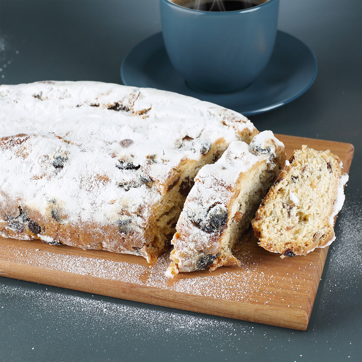 Nahaufnahme von angeschnittenem Rosinenstollen mit Puderzucker, Sultaninen und Mandeln auf Holzbrett