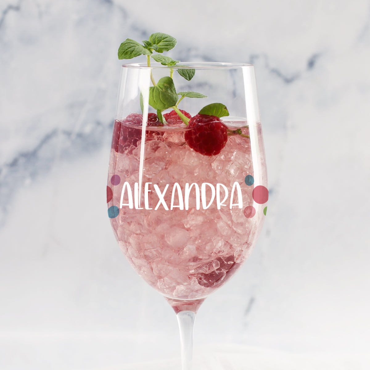 Personalisiertes Weinglas mit bunten Punkten und Name „Alexandra“, gefüllt mit rosa Getränk, Eis, Himbeere und Minze