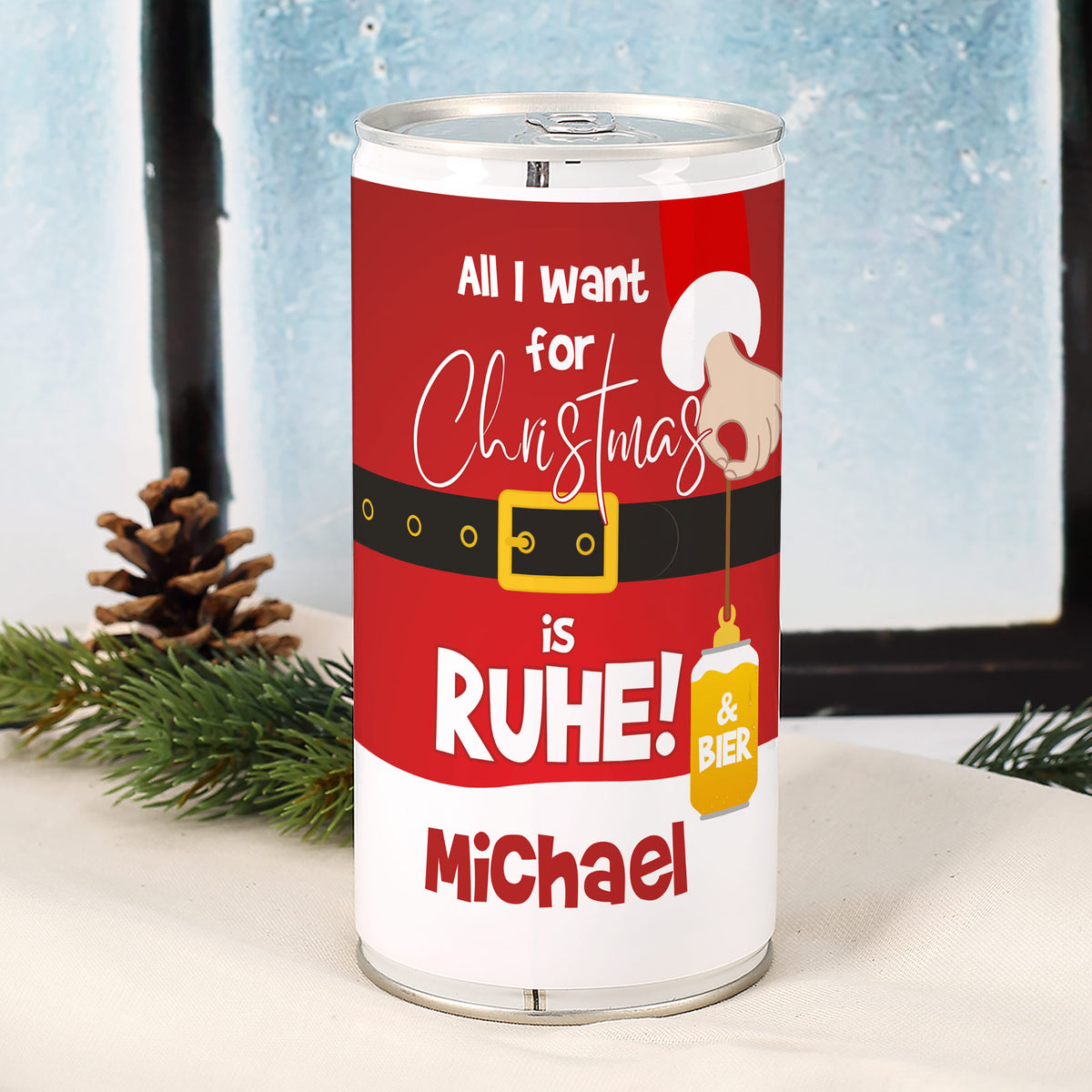 Personalisierte Weihnachtsbier-Dose mit rotem Weihnachtsmann-Design, Spruch „All I want for Christmas is Ruhe & Bier“ und individuell bedrucktem Namen, fotografiert im weihnachtlichen Setting mit Tannenzweig.