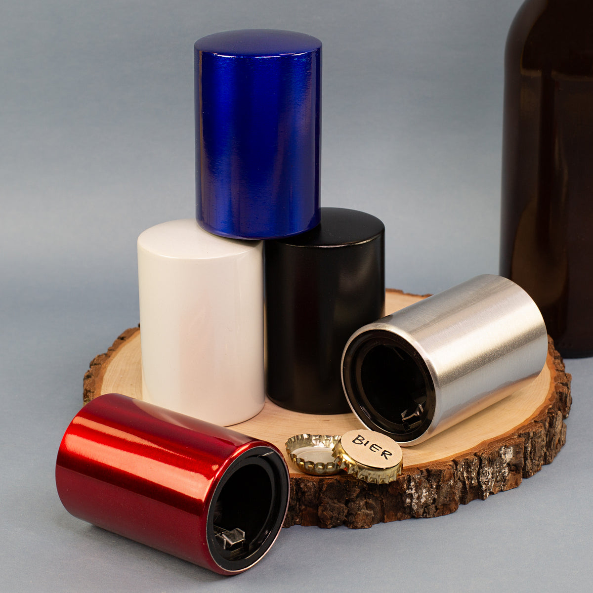 Mehrfarbige Push-Up Flaschenöffner aus Metall in Blau, Weiß, Schwarz, Silber und Rot auf Holzscheibe