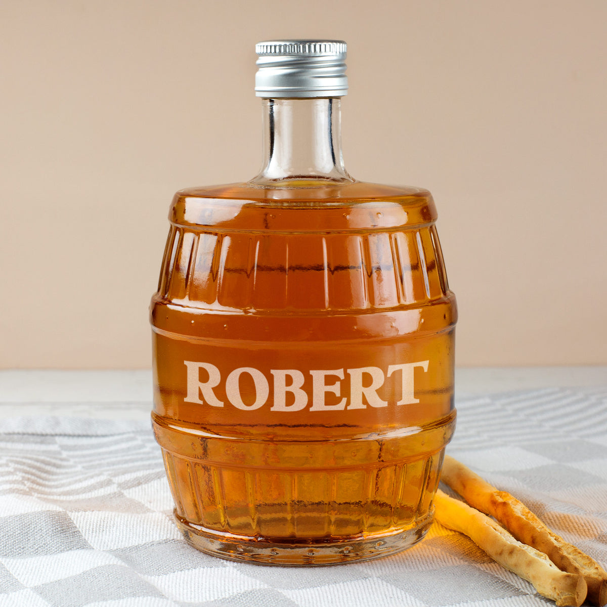 Glasflasche in Fassform mit Gravur ROBERT, befüllt mit Whisky, auf grauem Tuch