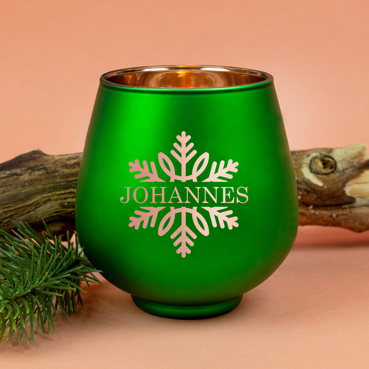 Grünes Windlicht mit Gravur „Johannes“ und Schneeflockenmotiv, dekorativ auf orangefarbenem Hintergrund mit Holzstück