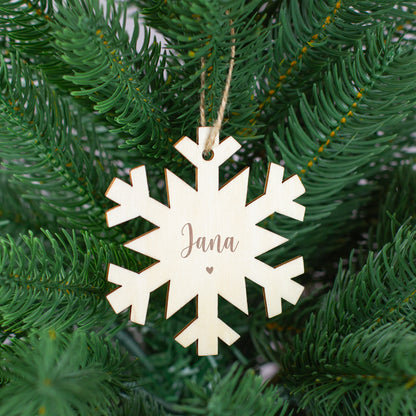 Schneeflocken-Holzanhänger mit Gravur „Jana“ und kleinem Herzmotiv, aufgehängt im Tannenbaum.