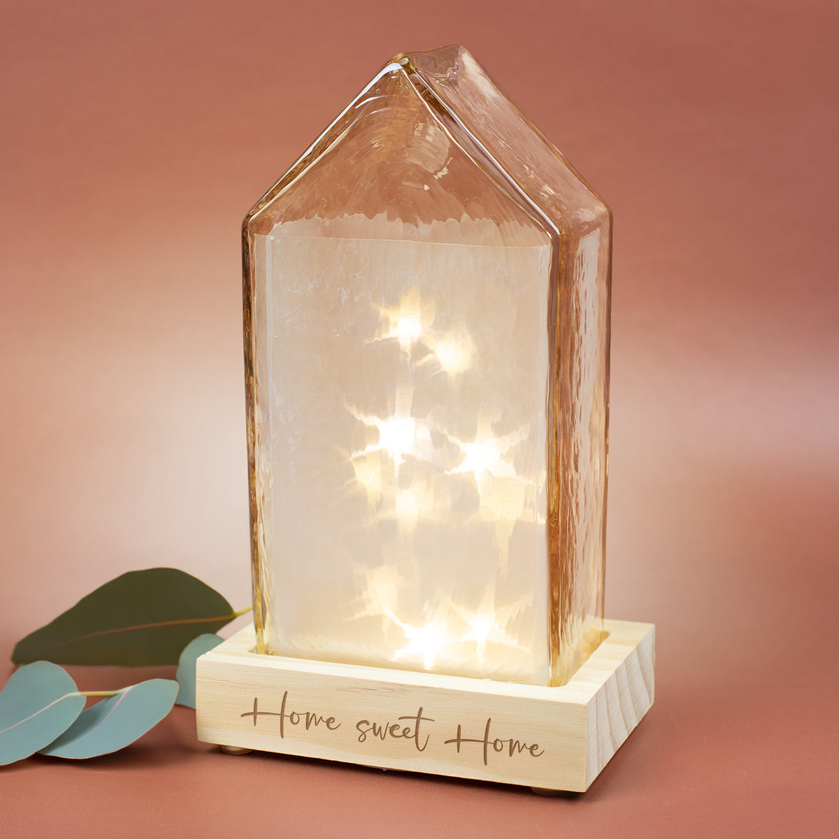 Amberfarbenes LED-Dekohaus von Leonardo auf Holzsockel mit graviertem Wunschtext – warm leuchtende Glashaus-Lampe als stimmungsvolle Wohn- und Geschenkdeko.