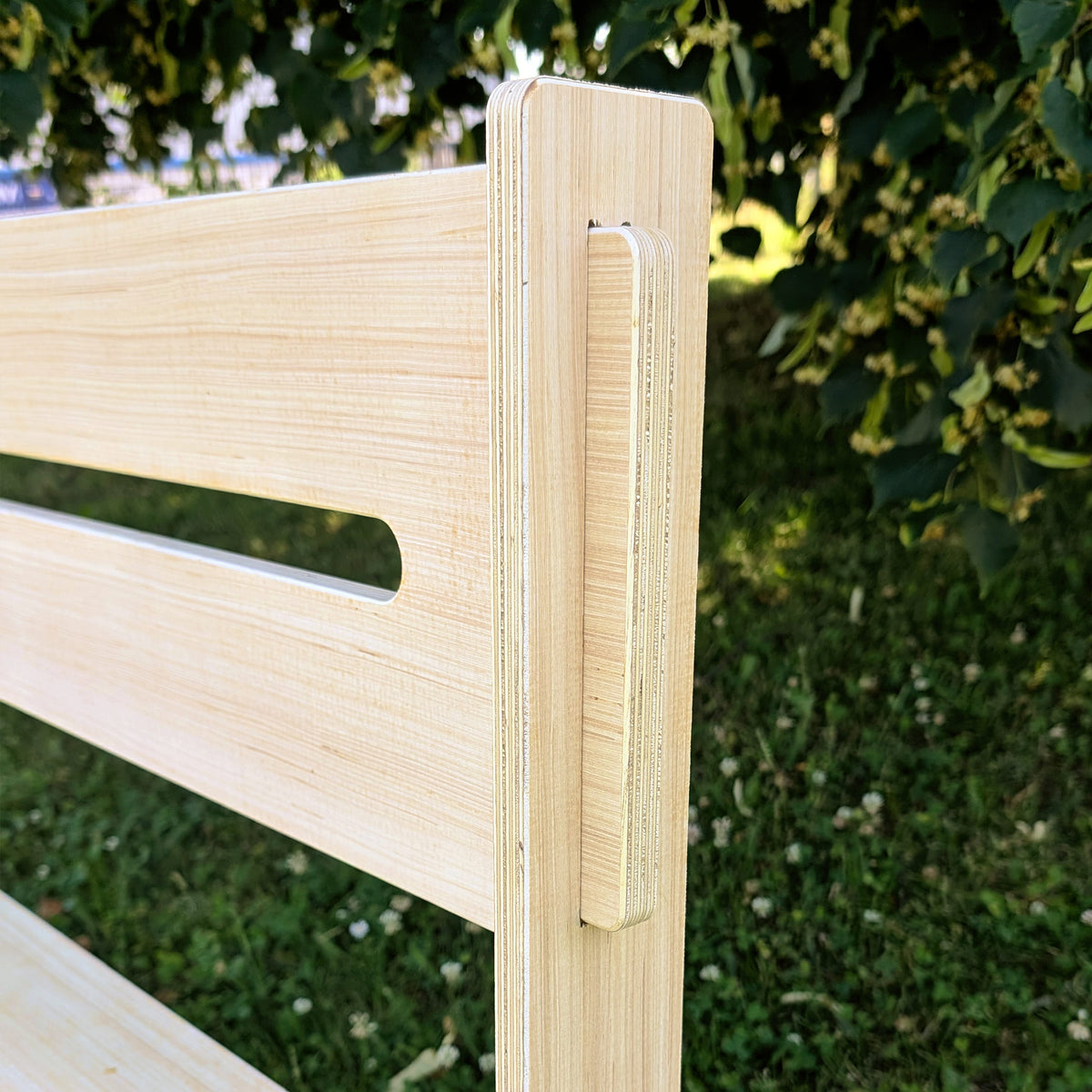 Detailansicht der präzise gearbeiteten Steckverbindung aus hellem Schichtholz an der Rückenlehne einer Holzbank im Freien