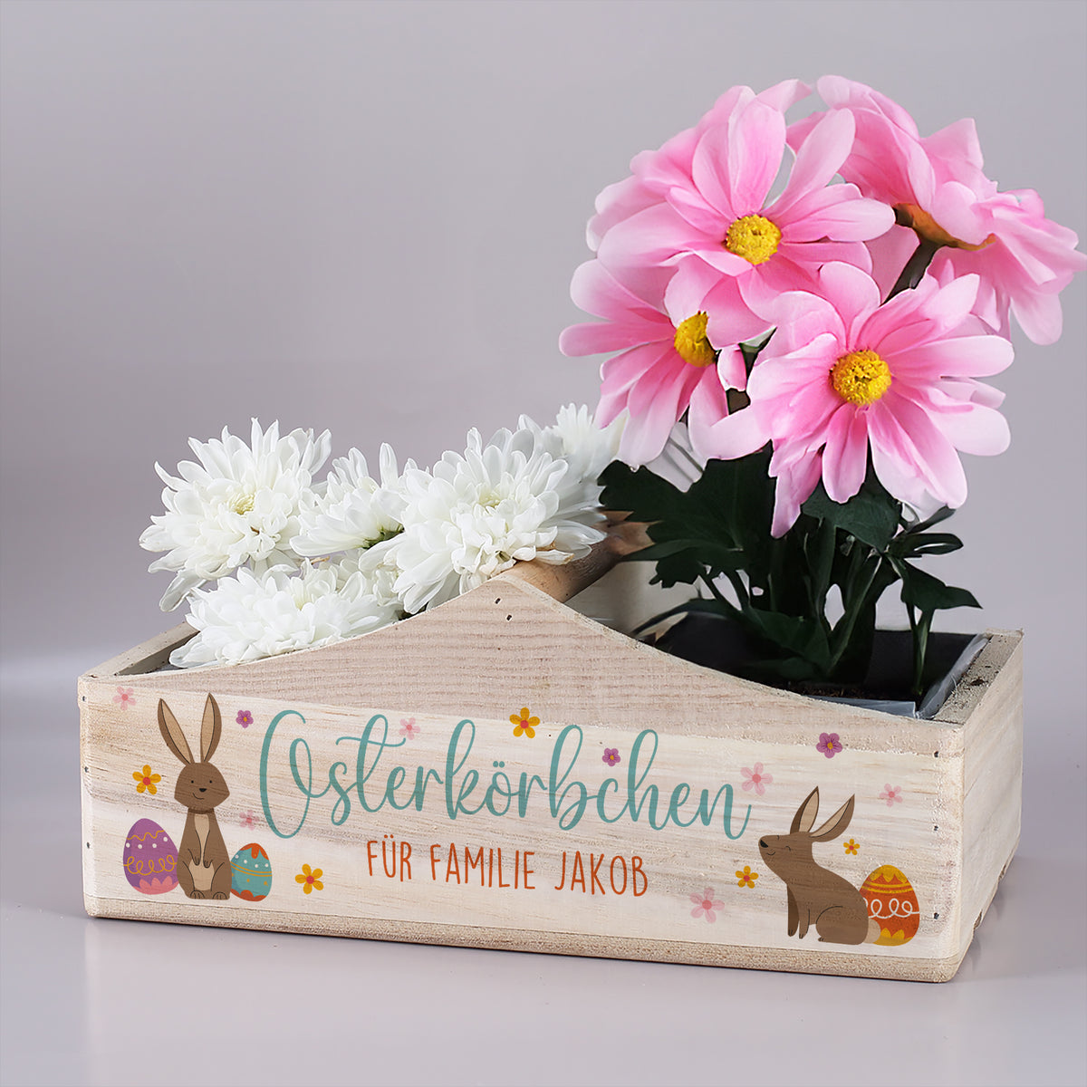 Osterkörbchen aus Holz mit Hasenmotiv und Wunschtext, bepflanzt mit Frühlingsblumen als Osterdekoration