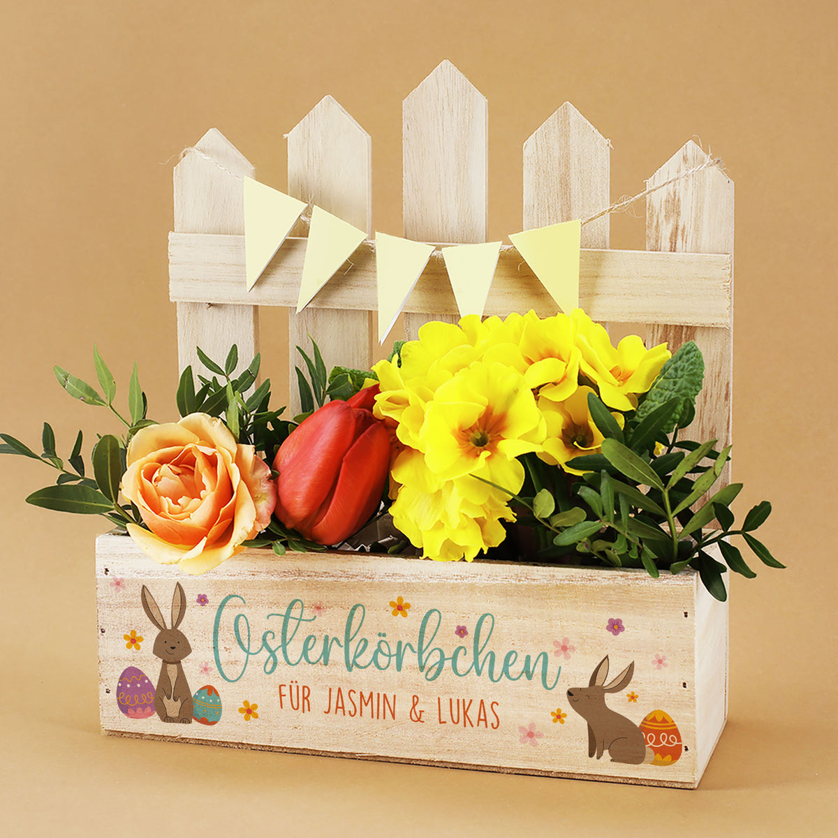Personalisierter Pflanzkorb aus Holz zu Ostern mit Zaun, Hasenmotiv und Aufdruck „Osterkörbchen“ mit Blumen dekoriert