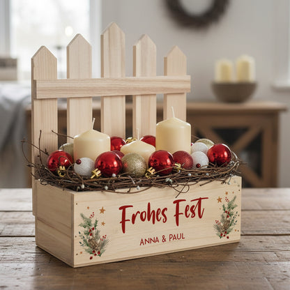 Weihnachtlich dekorierte Geschenkkiste mit Zaunelement, Kerzen und roten Christbaumkugeln auf einem Holztisch