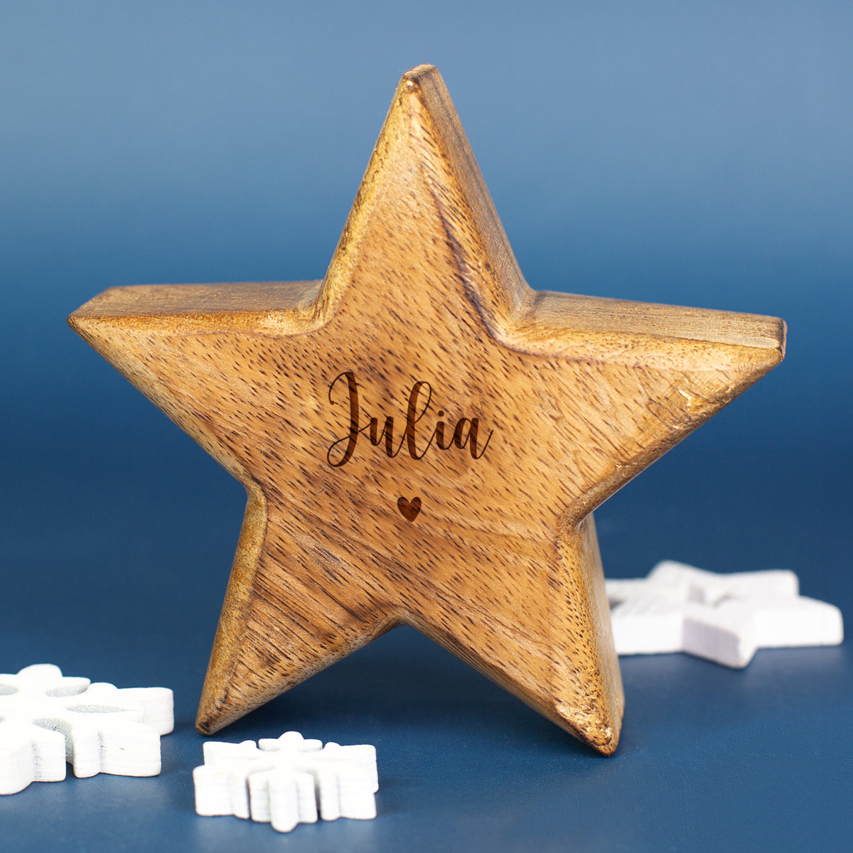 Holzstern mit Gravur „Julia“ als personalisierte Dekoration vor blauem Hintergrund mit Schneeflocken-Elementen