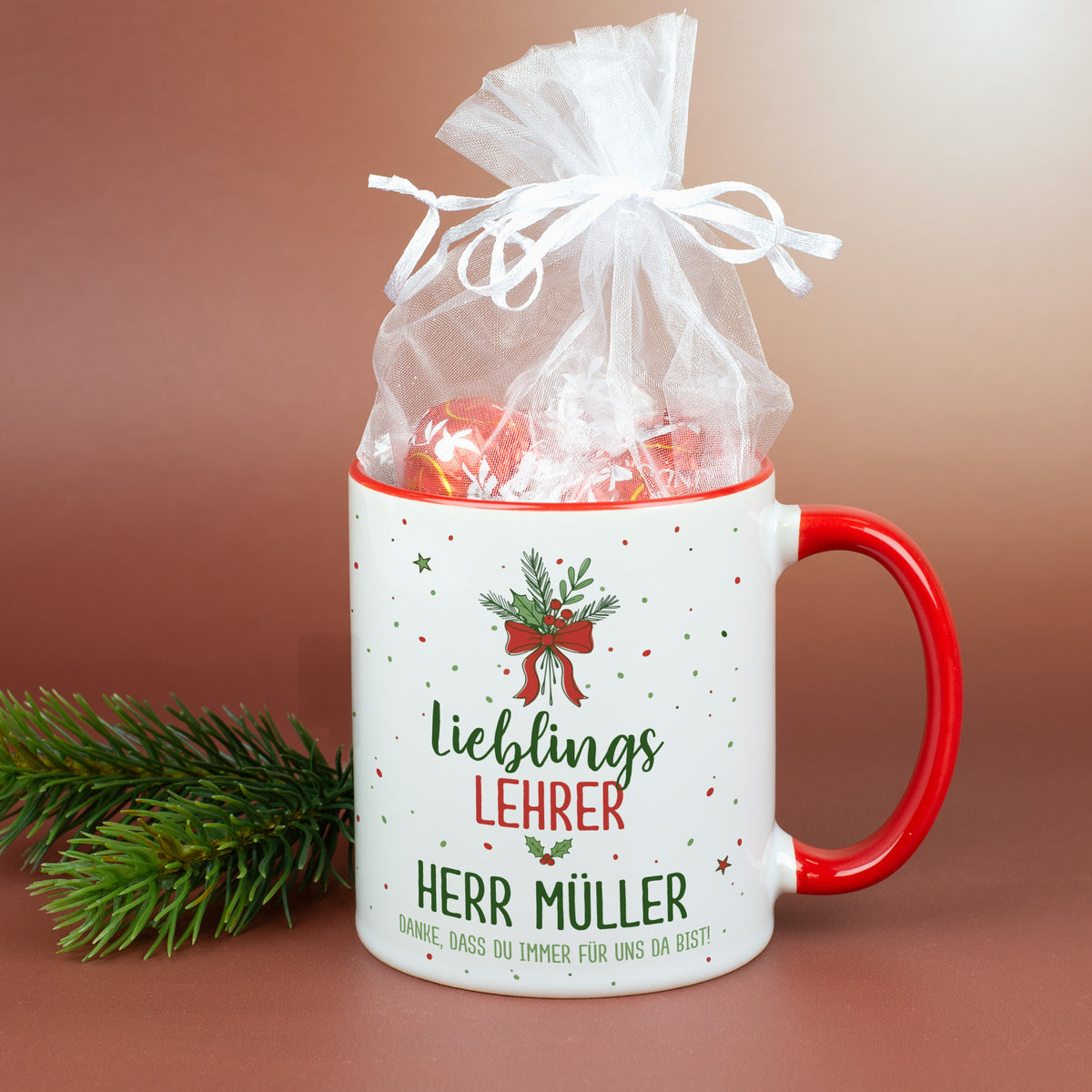 Weihnachtstasse mit rotem Henkel und festlichem Motiv für Lieblingslehrer, dekoriert mit Tannenzweig und Weihnachtskugeln.
