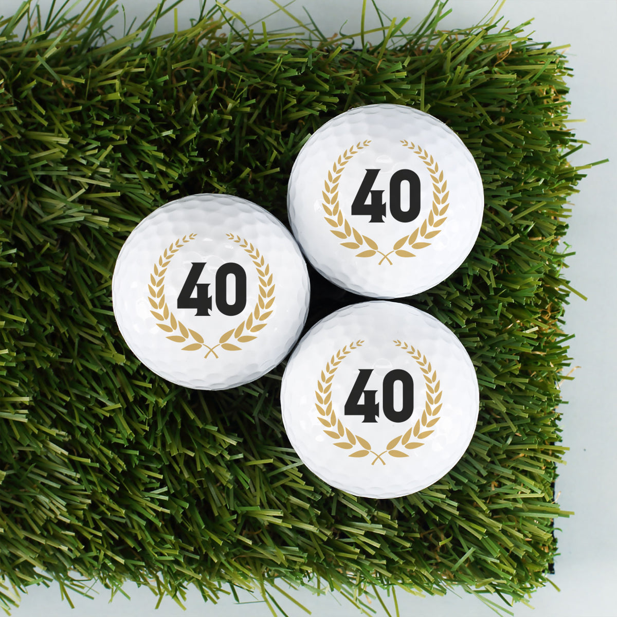 Drei personalisierte Golfbälle mit Zahl 40 im Lorbeerkranz auf Kunstrasen