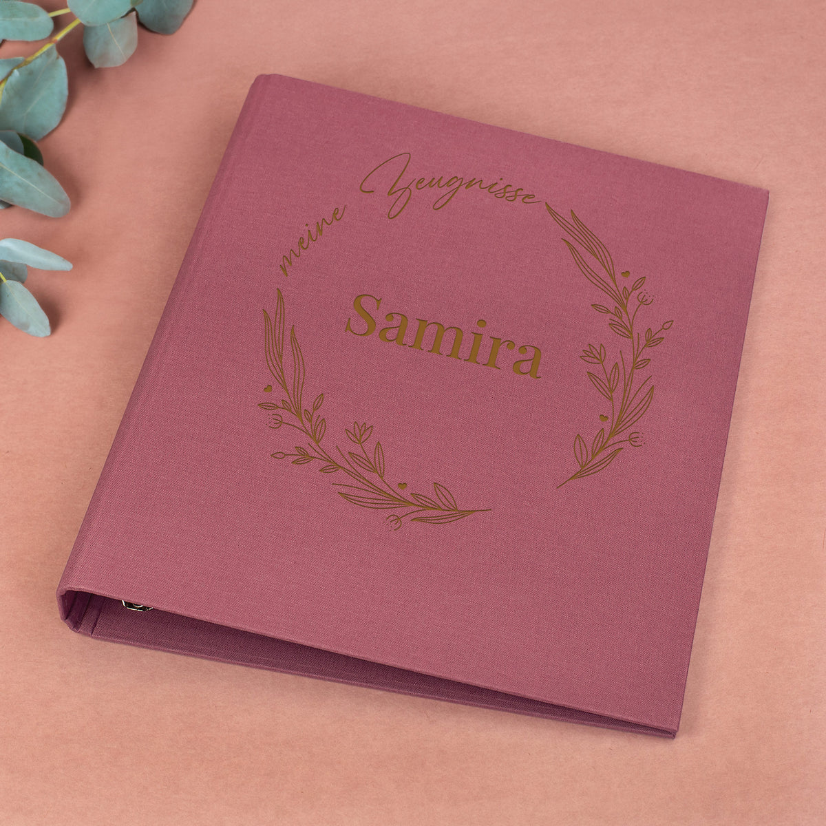 Rosafarbene Zeugnismappe aus Leinen mit floralem Lineart-Ring, Aufdruck „meine Zeugnisse“ und Name „Samira“.