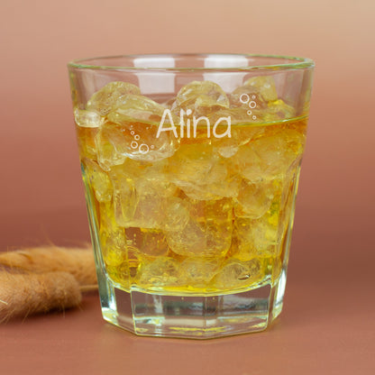 Leonardo-Trinkglas mit Gravur von Name und Blubberblasen-Motiv, gefüllt mit Apfelsaft und Eiswürfeln, auf hellem Holz – fröhliches Kinder- und Familienglas aus Glas.