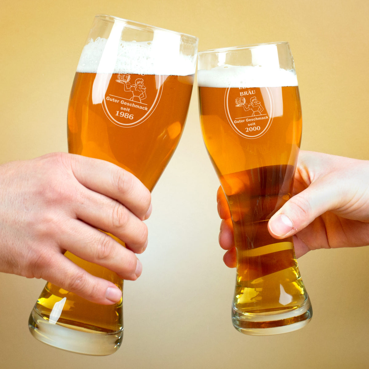 Zwei Hände stoßen mit gravierten Weizengläsern an, Gravur mit Bräu-Logo, Name und Jahr personalisiert