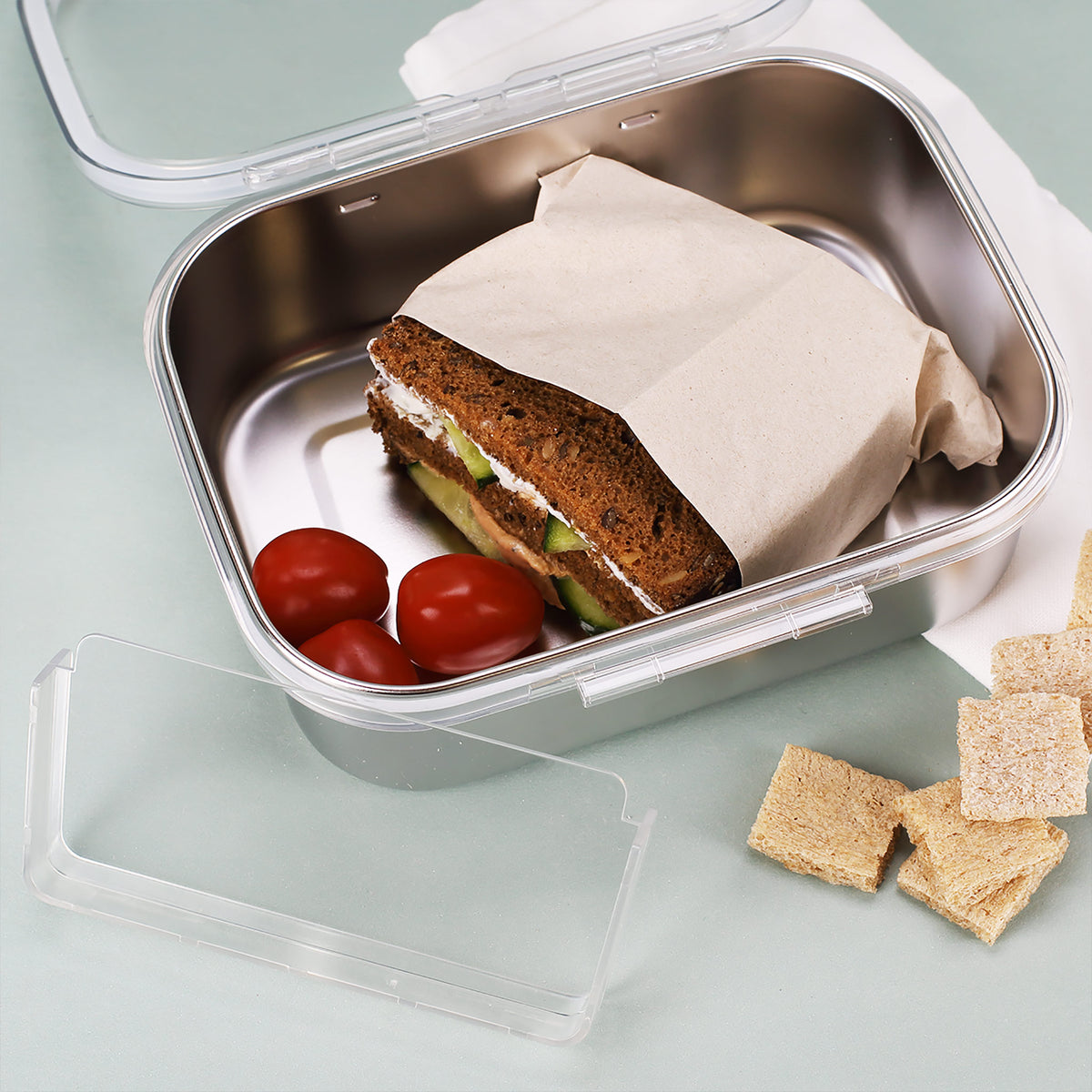 Brotdose aus Edelstahl offen mit belegtem Sandwich und Tomaten