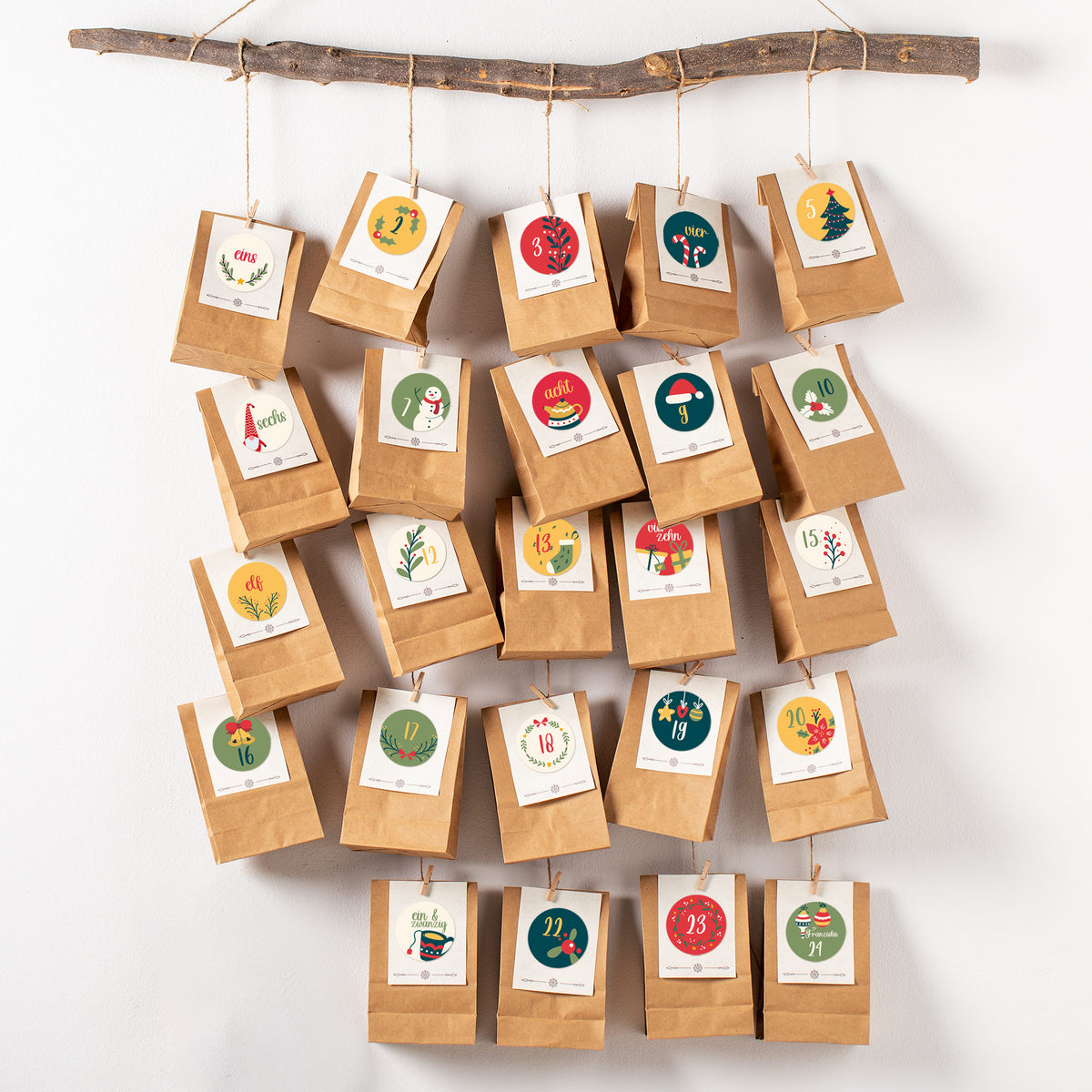 Selbstgemachter Adventskalender mit 24 Tüten und bunten Weihnachtsstickern an einem Ast aufgehängt