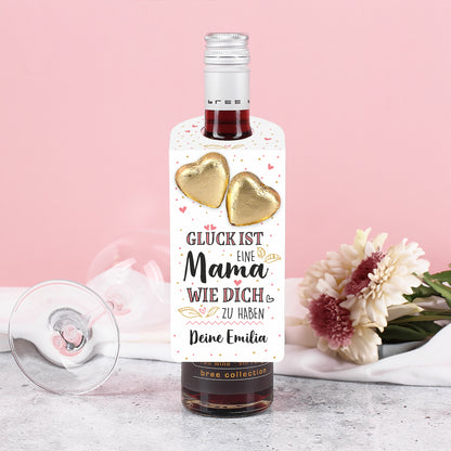 Rote Weinflasche mit Muttertagsanhänger, Text „Deine Emilia“ und zwei Lindt-Herzen, daneben Blumen und Weinglas