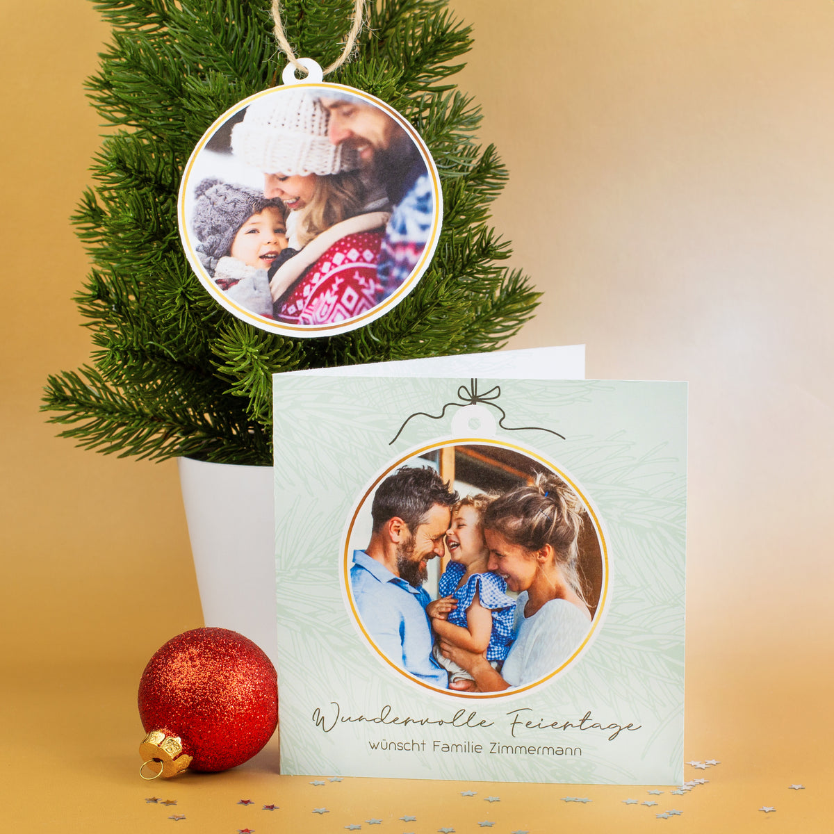 Aufgestellte Weihnachtskarte mit Familienfoto und herausnehmbarer Fotokugel, die an einem Mini-Tannenbaum hängt, im weihnachtlich dekorierten Setting