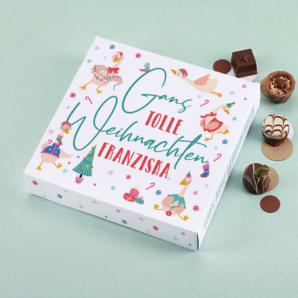 Lindt Pralinenbox mit Motiv „Gans tolle Weihnachten Franziska“, umgeben von Schokolade und Pralinen auf mintgrünem Hintergrund.
