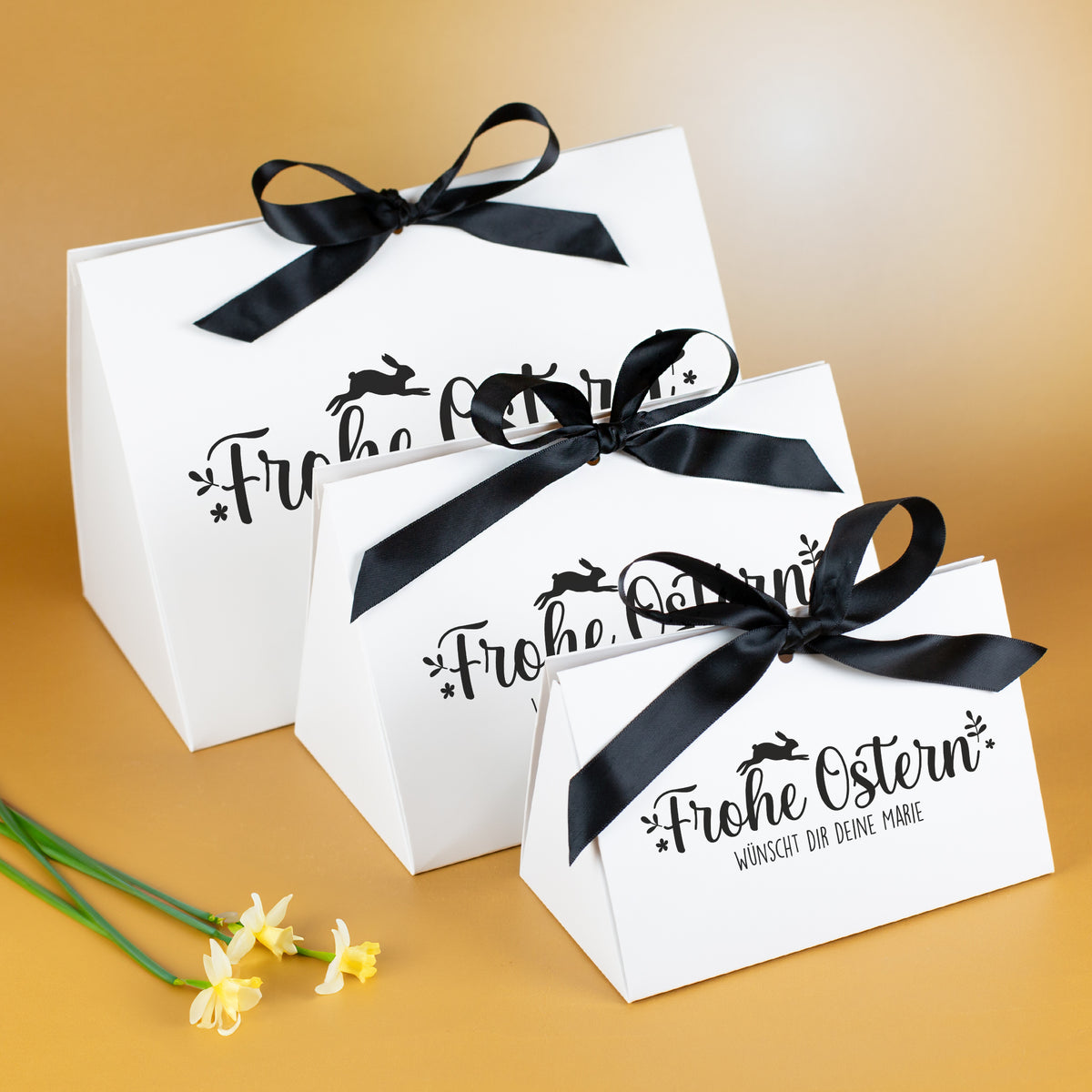 Drei weiße Oster-Geschenkverpackungen mit schwarzer Schleife und Frohe Ostern Motiv