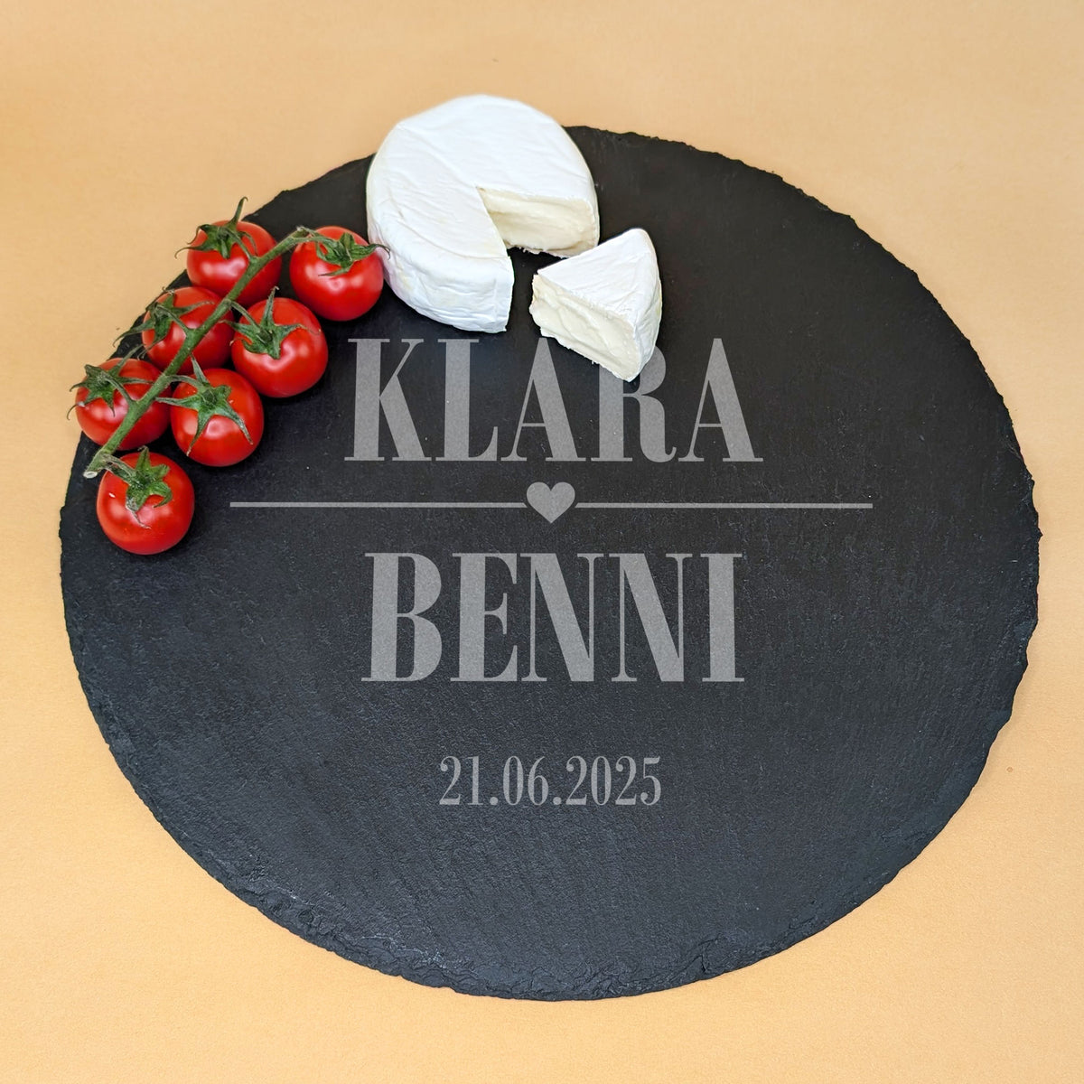 Personalisierte Schieferplatte mit Herz-Motiv Gravur, zwei Namen und Datum, dekoriert mit Käse und Tomaten.