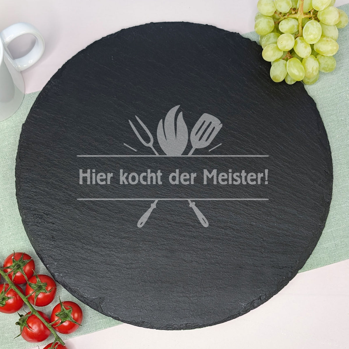 Personalisierte Schieferplatte mit Grillbesteckmotiv und einem Wunschtext, dekoriert mit Weintrauben, Tomaten und Kaffeetasse.
