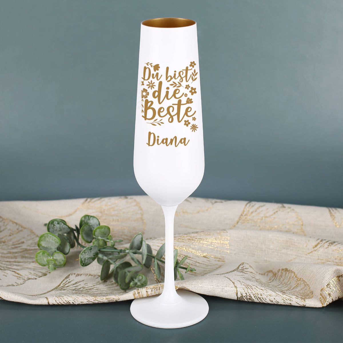 Personalisierbares Sektglas mit goldener Gravur „Du bist die Beste Diana“ – auf hellem Tisch mit Eukalyptus-Zweig