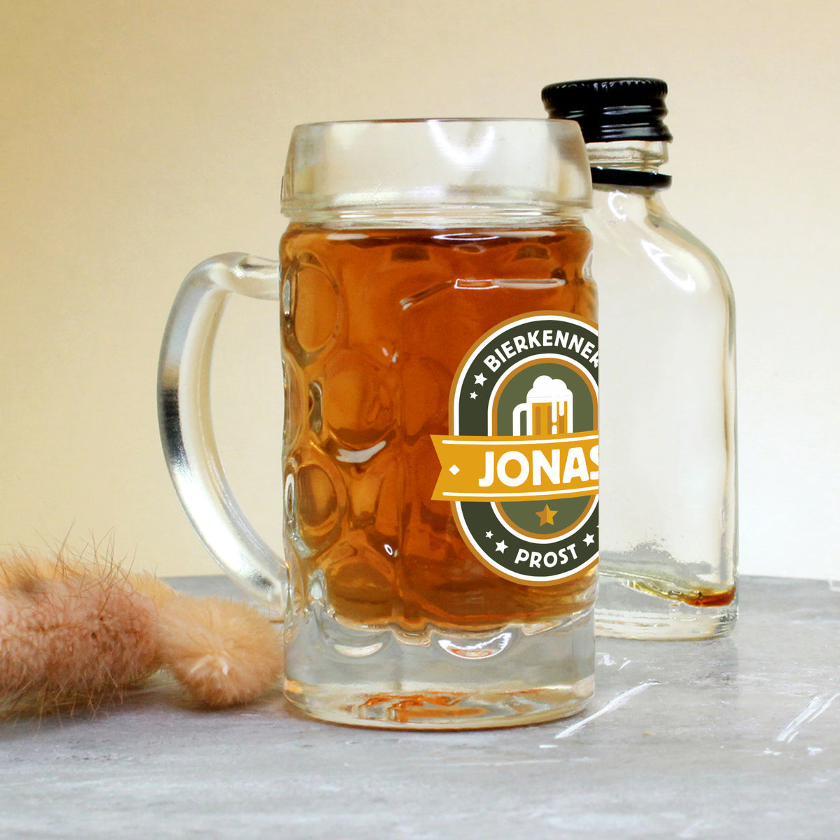 Mini-Bierkrug mit Henkel und 4 cl Inhalt, rechts im Bild eine kleine Likörflasche, vorn der Namensaufdruck „Jonas“ im Bierkenner-Design – eignet sich perfekt als Gag-Geschenk oder Ergänzung zu Männerpräsenten