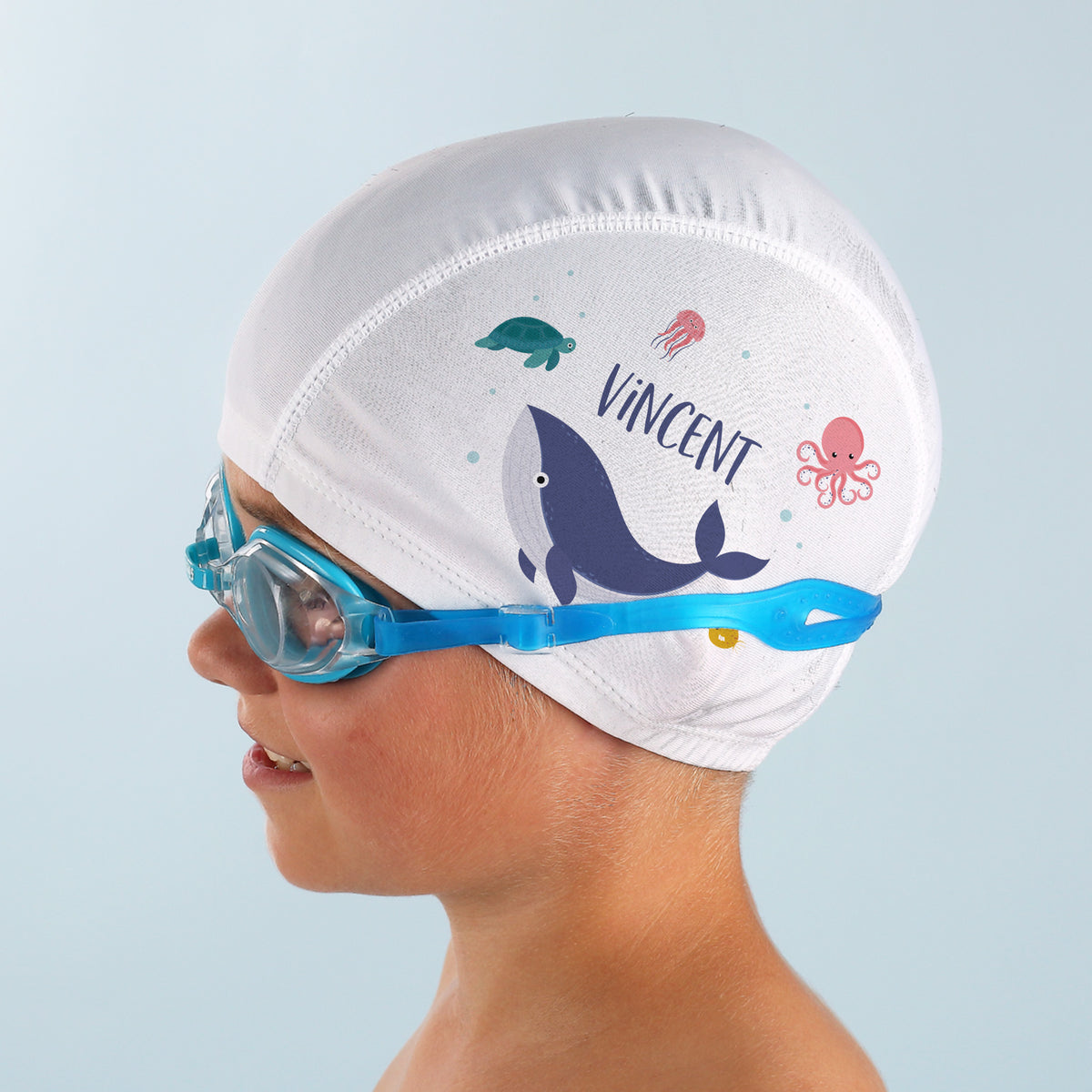 Kind mit Schwimmbrille trägt Badekappe mit Name und Meerestieren seitlich