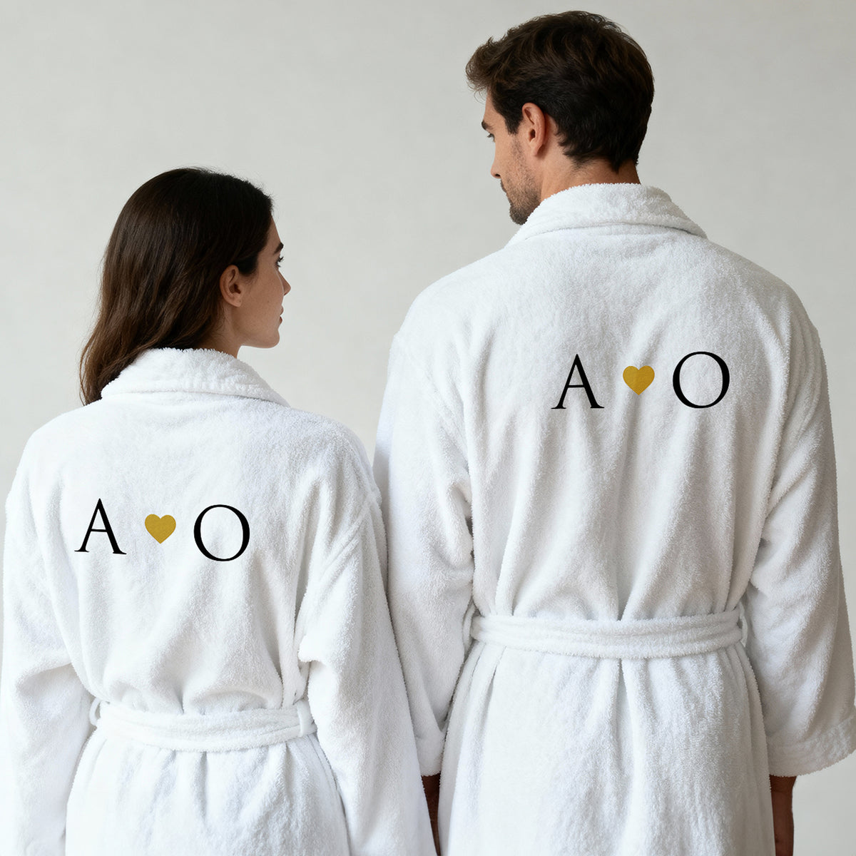 Paar in weißen Bademänteln von hinten, Initialen mit goldenem Herz bestickt, personalisiertes Partner-Set