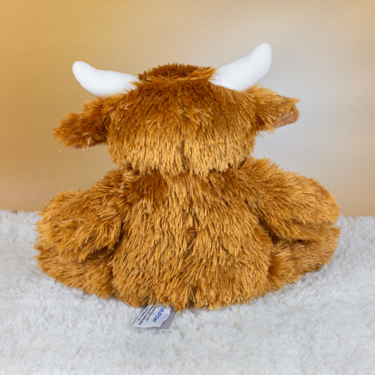 Rückansicht der flauschigen Kuscheltier-Kuh mit braunem Fell und weißen Hörnern.